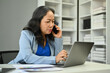 © Prathankarnpap - Professional 50s businesswoman having phone conversation and using laptop at desk.