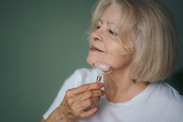 Beautiful senior woman with short hair holding a massager in her hand and using on face. Spa technique skincare ads.