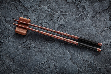 Classic Red Wooden Choppingsticks On Rest And Black Stone Background.