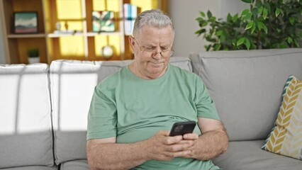 Sticker - Middle age grey-haired man using smartphone sitting on sofa at home