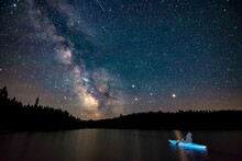 Person In Kayak Watching Night Sky With Stars In Distance