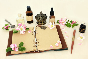 Wall Mural - Apple blossom flower preparation for natural herbal medicine remedies with notebook, essential oil bottles. Floral nature alternative healthcare concept on hemp paper.