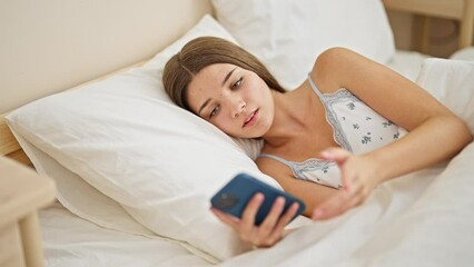 Sticker - Young beautiful girl using smartphone lying on bed looking upset at bedroom