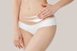 © Mirrorstudio - Young skinny girl in white lingerie on beige background applies cream on her belly