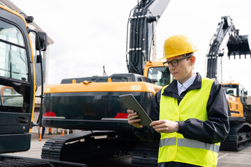 Aufkleber - Engineer in a helmet with a digital tablet stands next to construction excavators.