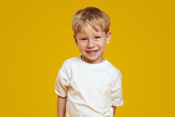 happy little blonde male kid boy in white tshirt laughing at camera against orange background