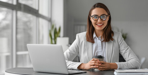 Canvas Print - Young businesswoman with cup of coffee sitting at table in office