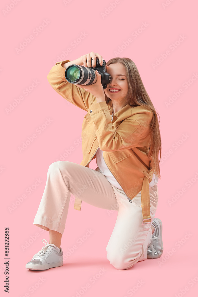 Young female photographer with professional camera on pink background