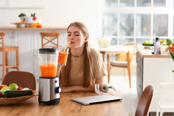 Wall Mural - Young woman drinking healthy smoothie in kitchen