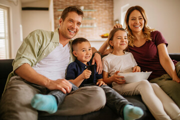 Young family watching the tv on the couch in the living room at home