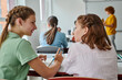 © LIGHTFIELD STUDIOS - Smiling teenage pupil talking to classmate and pointing with finger during lesson in classroom