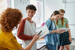 © LIGHTFIELD STUDIOS - Smiling schoolboy with braces holding notebook near friends with devices in classroom in school