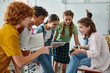 © LIGHTFIELD STUDIOS - Smiling teen pupils using digital tablet together in classroom near blurred african american teacher