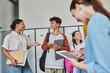 © LIGHTFIELD STUDIOS - african american teacher gesturing and talking with student, teenagers in school hallway with devices