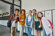 © LIGHTFIELD STUDIOS - cheerful teenage students holding devices and looking at camera in school hallway, teen friends