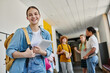 © LIGHTFIELD STUDIOS - teenage girl with digital tablet looking at camera in school hallway, blurred background, students