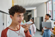© LIGHTFIELD STUDIOS - teenage schoolboy recording voice message, holding smartphone during break in school hallway, blur