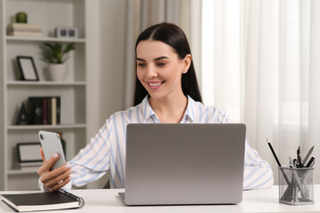 Canvas Print - Happy woman with smartphone working on laptop at white desk in room