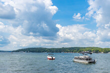 A pontoon boat and pleasure boat anchored in a large lake with white cumulus clouds and a blue sky.