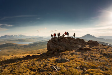 Big diverse group of hikers silhouettes stands at mountain top and looks at sunset