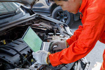 Young Asian mechanic in orange uniform View on laptop about car engine while repairing in garage