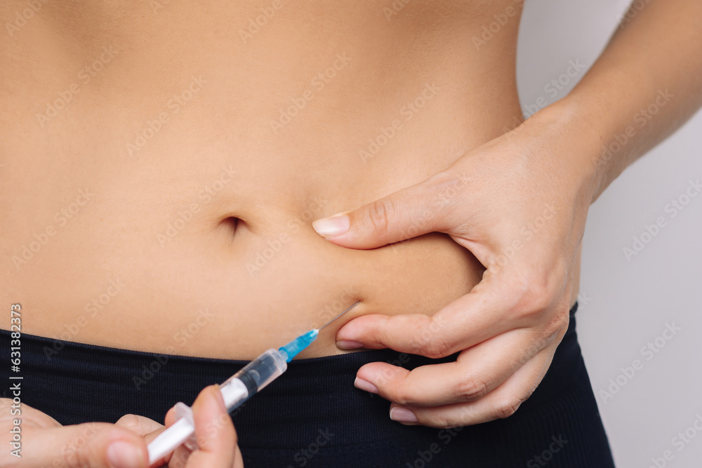 Cropped shot of a young woman putting a hormonal injection in her stomach with the syringe. The use of lipolytics in cosmetology. Anticoagulant injections. Preparations for figure correction. Close up