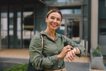 Wall Mural - Woman freelancer looking on her wrist watch standing on modern office building background