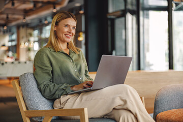 Wall Mural - Stylish woman freelancer working on laptop in cozy coworking and looking at side