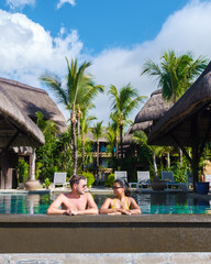 Wall Mural - Man and Woman relaxing in a swimming pool, a couple on a honeymoon vacation in Mauritius tanning in the pool with palm trees and sun beds at a sunny day