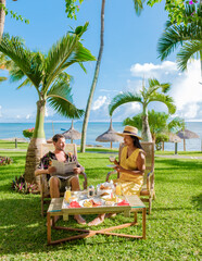 Wall Mural - Man and Woman having breakfast in a garden with palm trees on a tropical beach in Mauritius, a couple on a honeymoon vacation in Mauritius