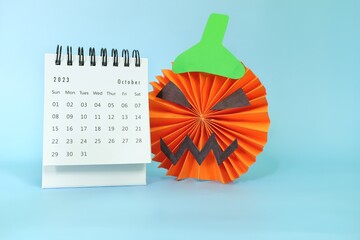 Wall Mural - Selective focus of October 2023 desk calendar  with jack o lantern pumpkin decoration on blue background with copy space. Halloween celebration.