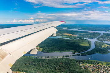 View of airplane wing, blue skies and green land and river during landing. Airplane window view.