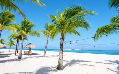 Le Morne beach Mauritius Tropical beach with palm trees, white sand blue ocean and beach beds with umbrellas, sun chairs,, parasols under a palm tree at Mauritius Le Morne with blue sky