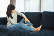 Young woman has problem with structural posture knee legs and ankle pain. Massage her legs for relief. reduce muscle tension on sofa couch in living room at home