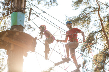 Adorable little girl enjoying her time in a rope playground structure at adventure park, her father supporting her, family weekend activities.