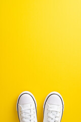 Foster healthy habits with the walk-to-school approach. Above view vertical picture of pair of clean white sneakers on sunny yellow isolated background, offering copyspace for advert or text placement