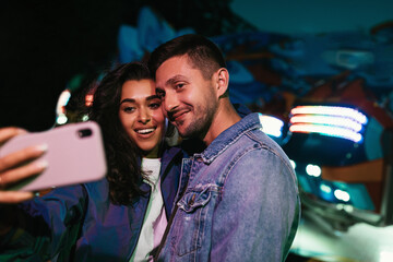 Young smiling people taking selfie at night in an amusement park