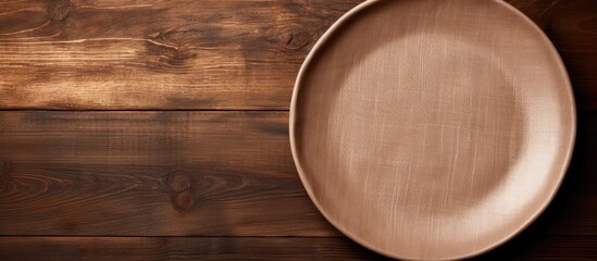 Poster - brown wooden background with an empty plate and a linen napkin on top. empty space available