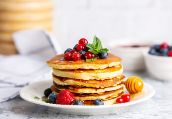 Wall Mural - Healthy summer breakfast, homemade classic american pancakes with fresh fruit and honey, morning light gray stone background copy space top view