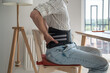 © DimaBerlin - Man freelancer works types on computer keyboard wearing back support belt corset on lower back during exacerbation to treatment of hernia. Back pain health problems as consequences of sedentary work.