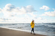 © maxbelchenko - Young woman tourist in a yellow coat walks along the seashore, enjoys the seascape at sunset. Travel, tourism concept. Active lifestyle.