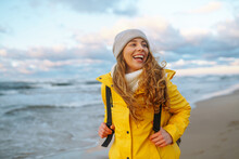 Young Woman Tourist In A Yellow Coat Walks Along The Seashore, Enjoys The Seascape At Sunset. Travel, Tourism Concept. Active Lifestyle.