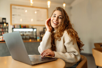 Wall Mural - Portrait of a young woman sitting in a cafe at a laptop, working online, freelancing. Сoncept of education, blog. Technologies.