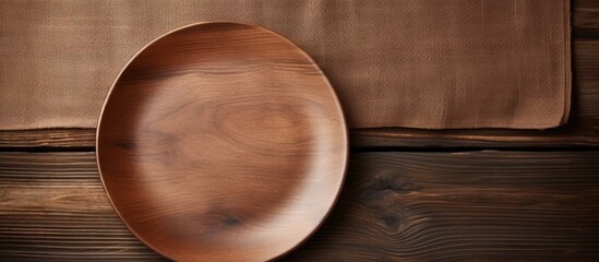 Poster - brown wooden background with an empty plate and a linen napkin on top. empty space available