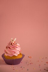 Poster - Appetizing cupcake with a pink frosting and decorative sprinkles on a pink surface