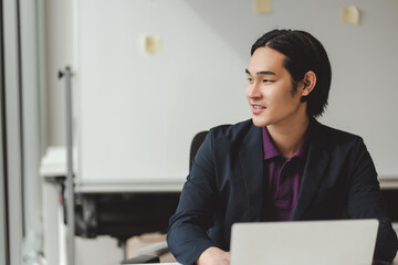 Portrait of smiling Asian man wearing formal wear, working at workplace, using laptop