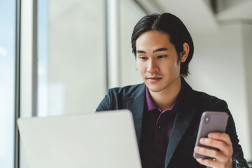 Portrait of positive asian student studying online, using laptop, checking mail holding mobile phone