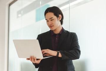 Portrait of attractive asian man standing in modern office holding, using laptop, working online