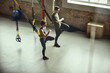 © Friends Stock - Exercising together. Young active couple in sportswear training legs with Trx fitness straps at gym.