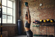 © Friends Stock - Bodybuilding. Side view of beautiful young woman with tattoo on er hand in sports clothing exercising with dumbbells while standing at gym.